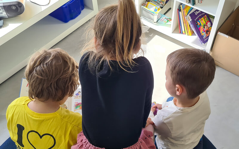 Drei Kinder sitzen auf einem grossen Kissen und lesen in einem Buch